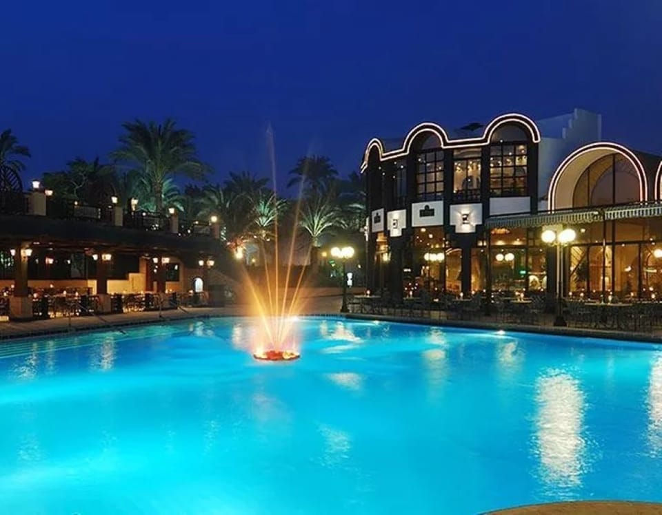 Unwind under glowing lights beside the sparkling fountain-lit pool
