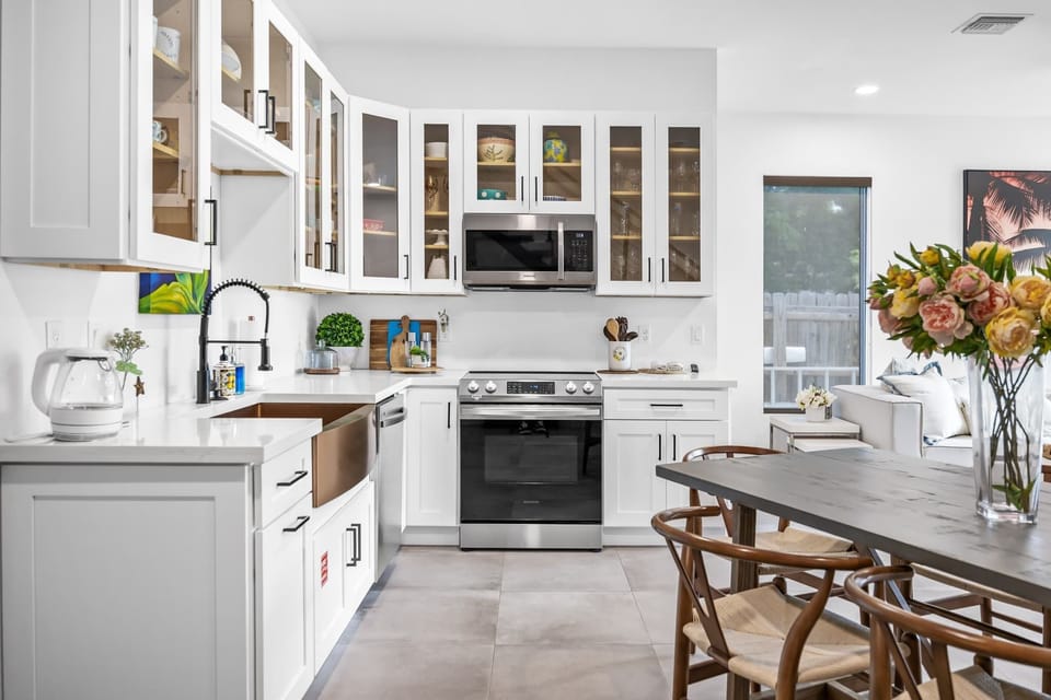 Modern kitchen with white cabinetry, stainless steel appliances, and a dining area with wooden chairs.