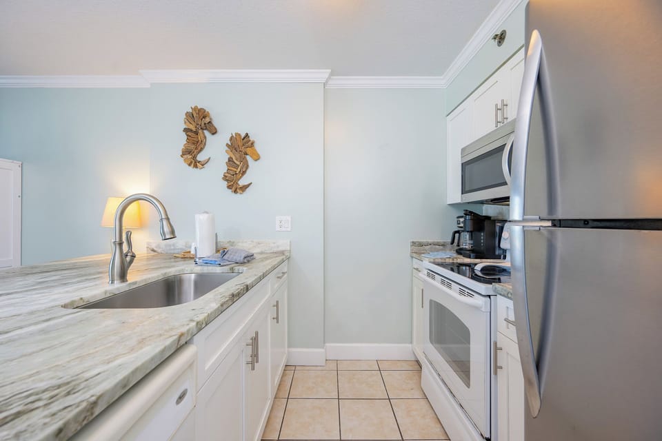 Modern kitchen featuring white and stainless appliances, marble countertops, and charming seahorse decor