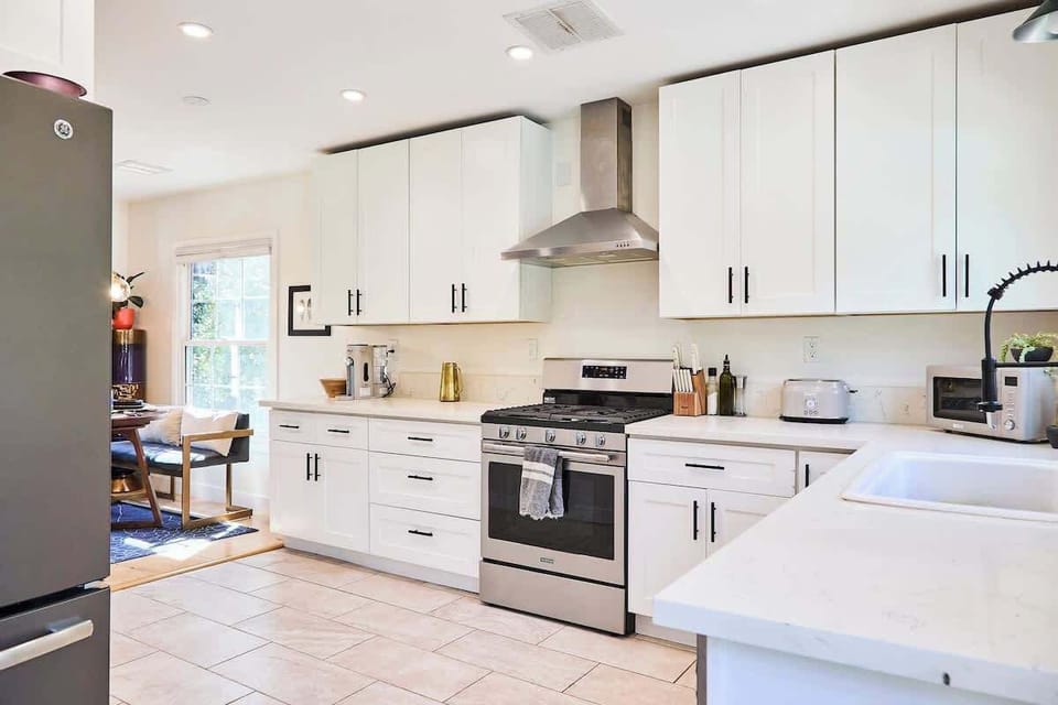 This spacious kitchen combines function and style with crisp white cabinetry, stainless steel appliances, and a sleek vent hood. The expansive countertops and modern fixtures provide plenty of prep space, seamlessly connecting to the dining area.