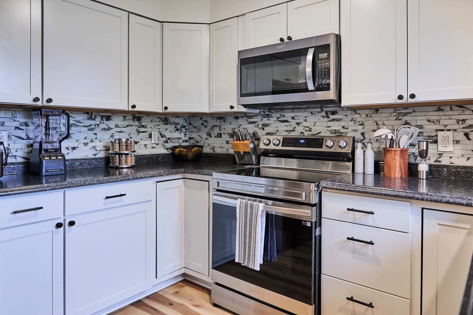 This updated kitchen features stainless steel appliances, white cabinets, and a bold mosaic tile backsplash. Granite countertops add durability and style, while the layout provides ample prep and storage space for home cooking.