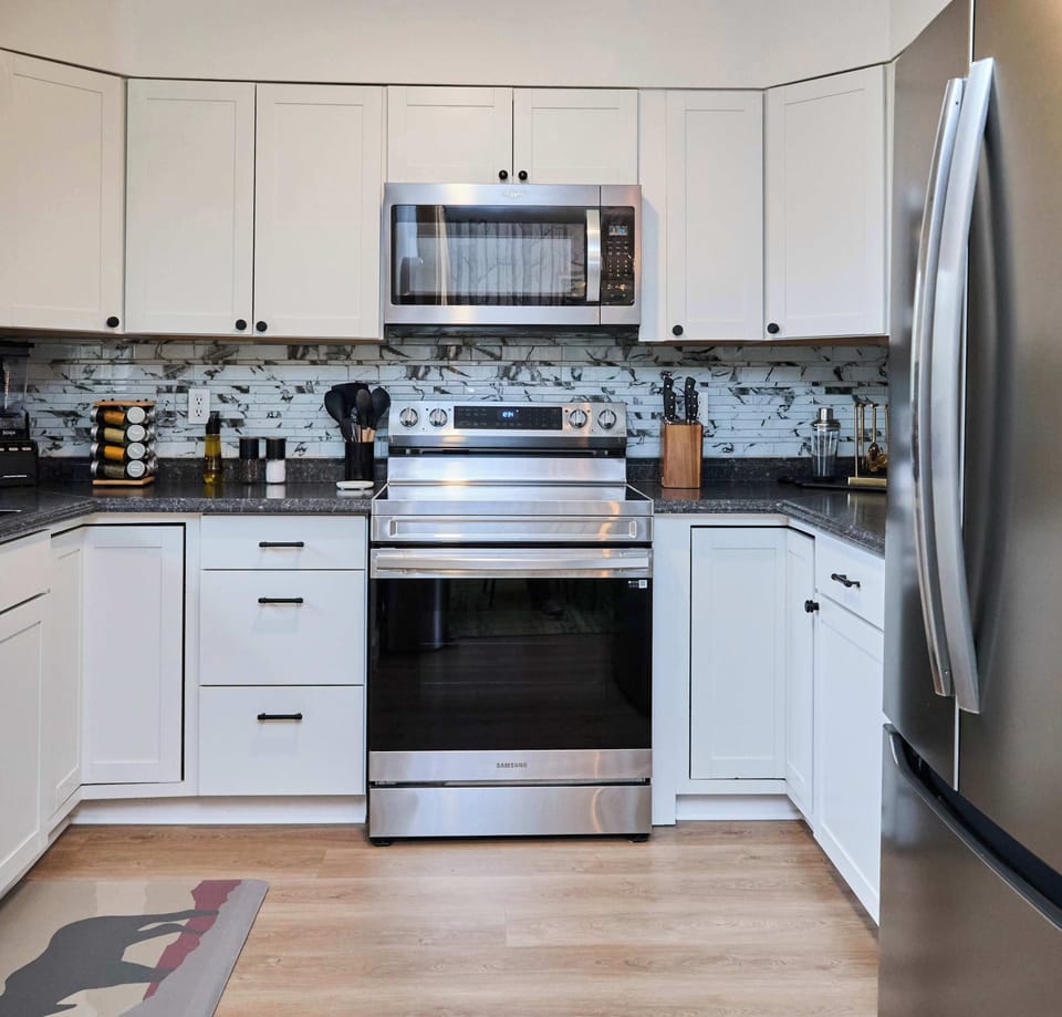 Cook with ease in the fully equipped kitchen featuring stainless steel appliances, a sleek backsplash, and spacious countertops. With a full-size fridge, oven, microwave, and modern essentials, this kitchen is ready for every meal.