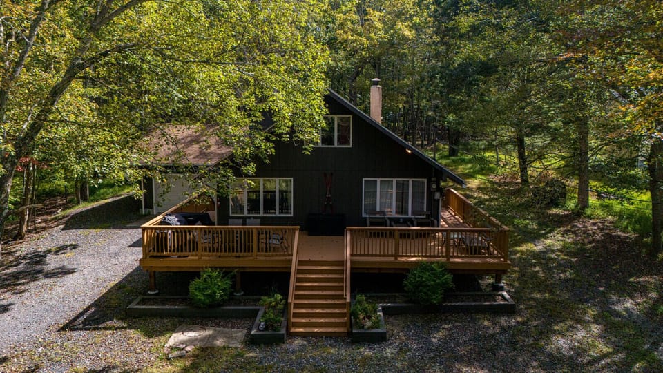 Charming Poconos cabin exterior with a large wooden deck, nestled in the trees for a private mountain escape.