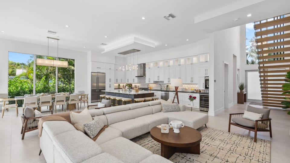 Bright & Modern Delray Beach Retreat – Spacious open-concept living with a designer kitchen, large island, and floor-to-ceiling windows showcasing lush tropical views. 