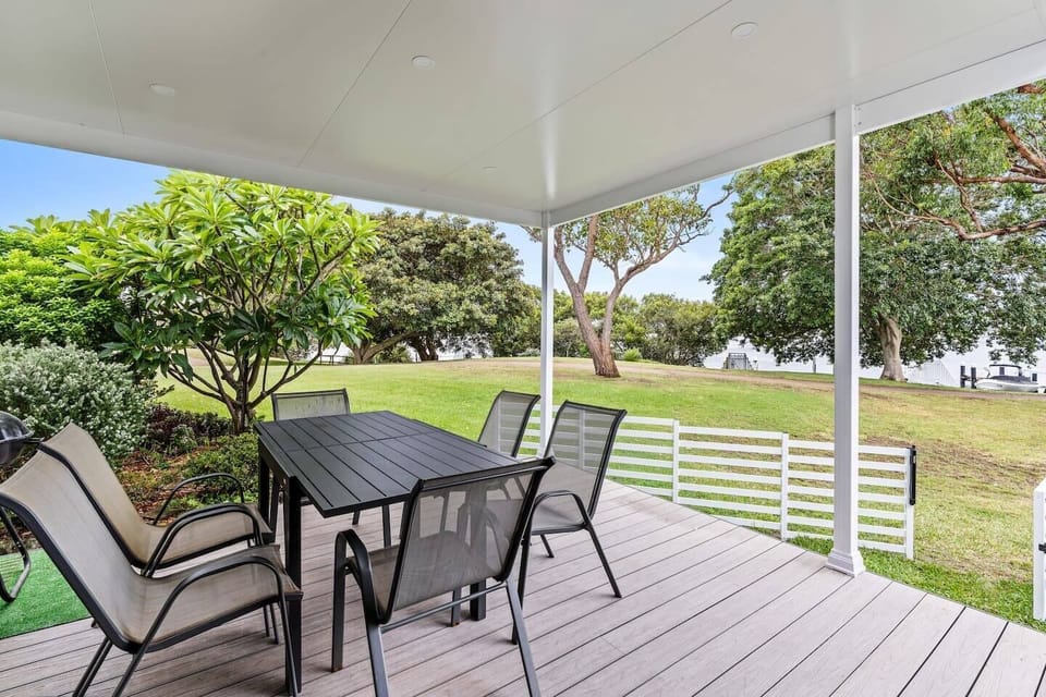 Dine alfresco on the covered front deck, with leafy gardens and breezy water views creating a peaceful outdoor retreat.