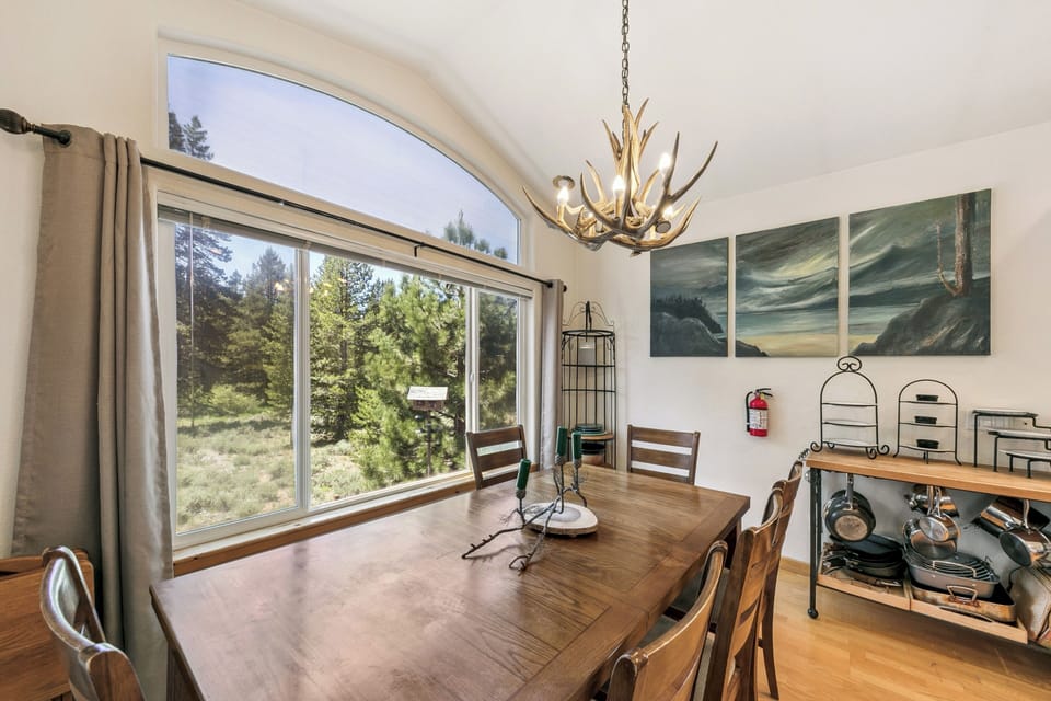 Gather around your rustic dining table beneath the antler chandelier, where panoramic forest views create the perfect backdrop for memorable meals together.