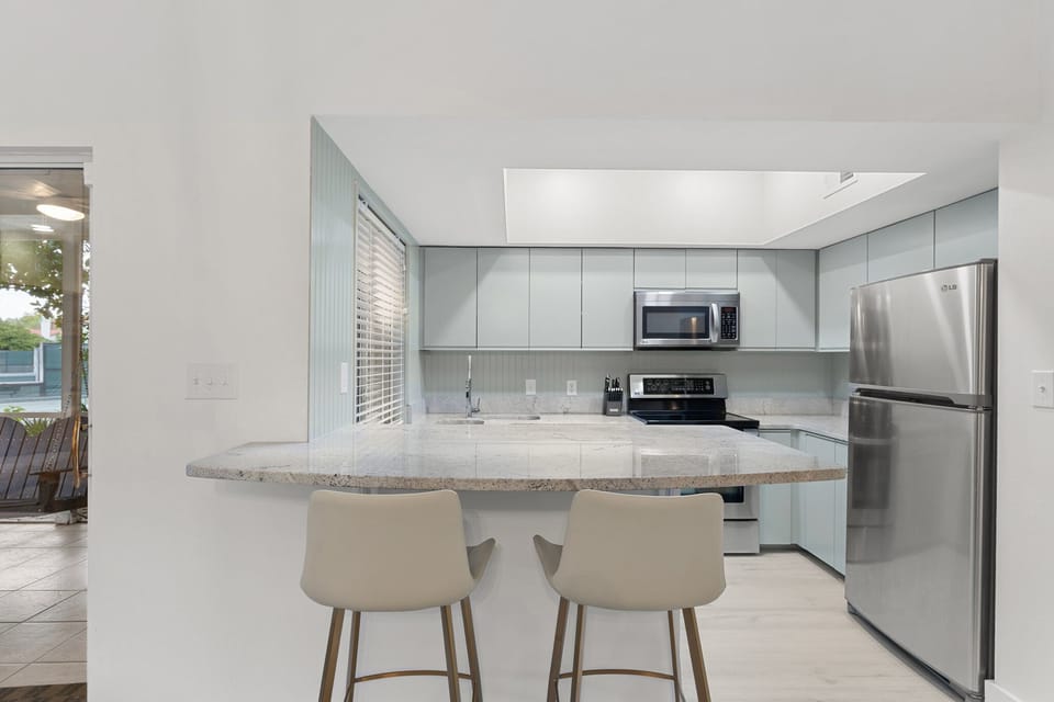 This modern kitchen features sleek appliances, soft coastal tones, and a bar perfect for morning coffee.