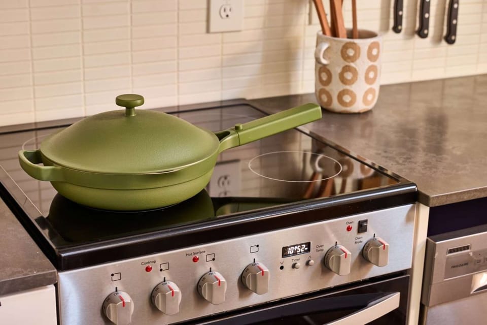 Green pan on electric stove with pot of utensils beside it