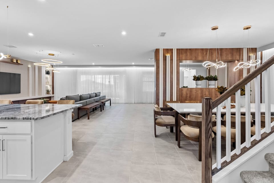 Experience a spacious living area with a stylish kitchen showcasing a polished granite countertop and a cozy wooden accent wall, perfect for both relaxation and entertaining, enhanced by modern light fixtures.