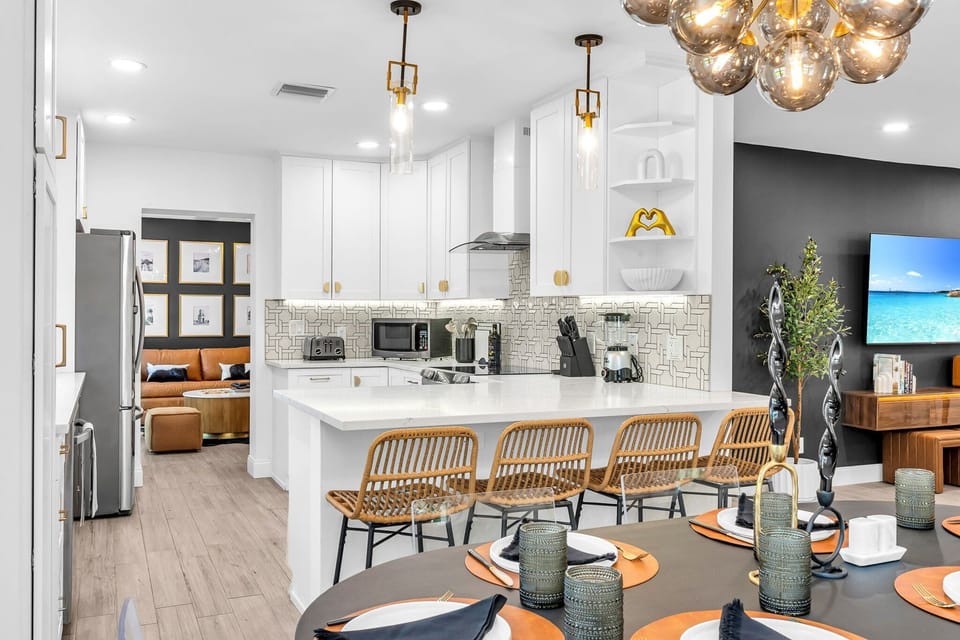 Modern open-concept kitchen and dining area with seating for 10—perfect for group stays and family gatherings. Features high-end finishes, rattan bar stools, and luxury lighting for a sleek Palm Beach vibe.