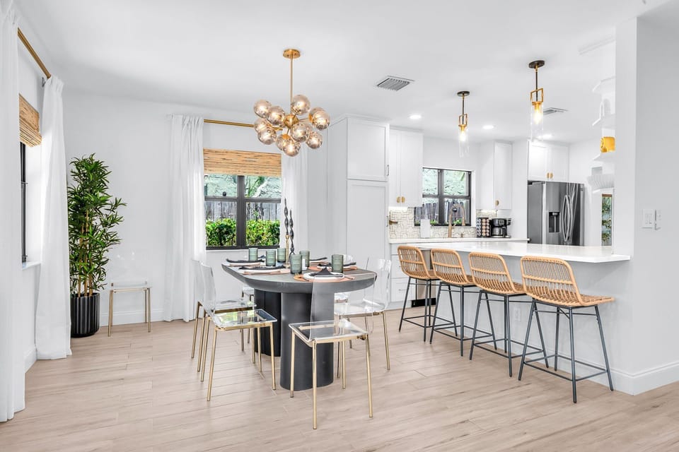 Modern open-concept kitchen and dining area with seating for 10—perfect for group stays and family gatherings. Features high-end finishes, rattan bar stools, and luxury lighting for a sleek Palm Beach vibe.