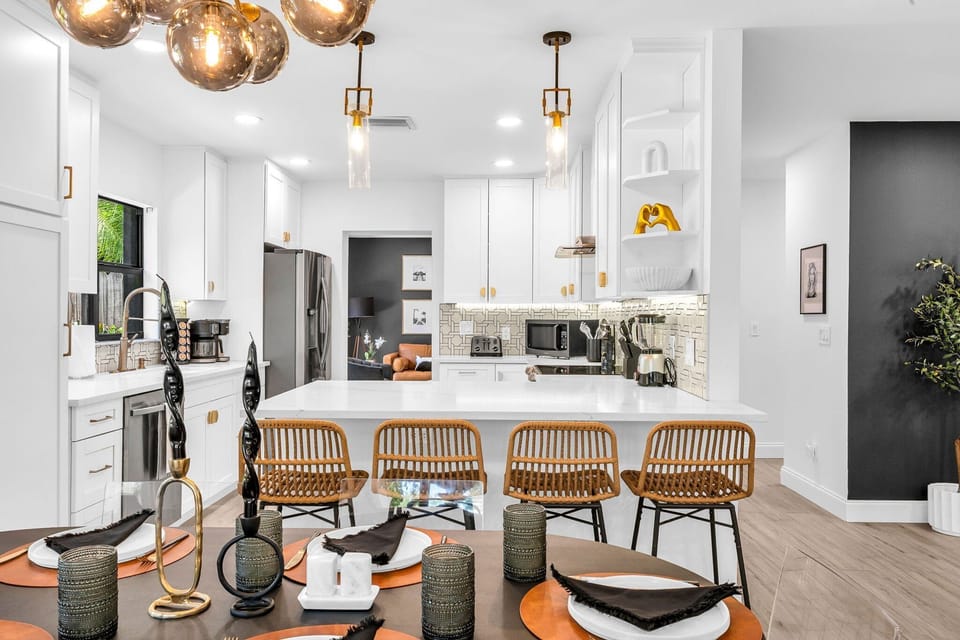 Modern open-concept kitchen and dining area with seating for 10—perfect for group stays and family gatherings. Features high-end finishes, rattan bar stools, and luxury lighting for a sleek Palm Beach vibe.