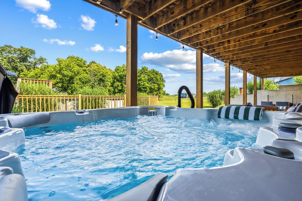 A bubbling private hot tub under a covered pergola with open Kentucky countryside views and string lights overhead. Pure relaxation awaits just steps from your back door.