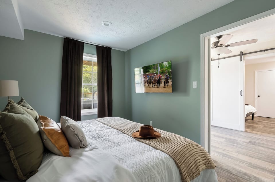 Sage green walls, a wall mounted smart TV and a sliding barn door entrance give this room a relaxed modern farmhouse feel that guests absolutely love. 🐎 Rest easy in bourbon country.