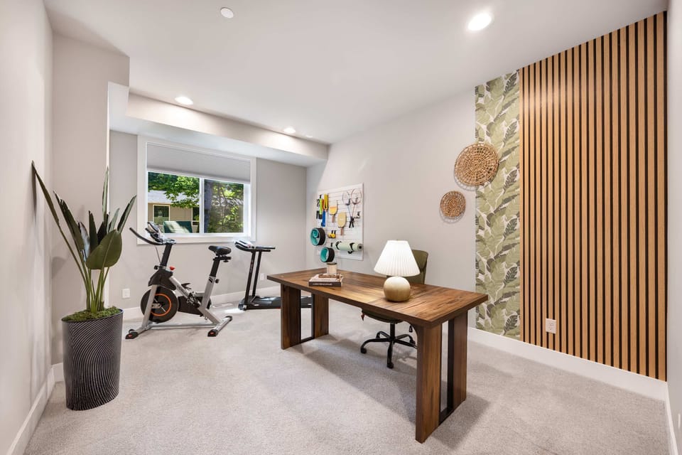 A versatile room with cardio equipment (spin bike, treadmill) alongside a wooden desk for remote work.