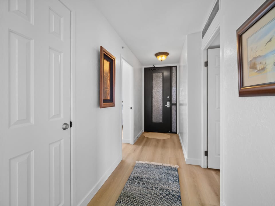 The inviting hallway features tropical-inspired art, wood flooring, and natural light—setting the tone for a relaxing Maui vacation experience.