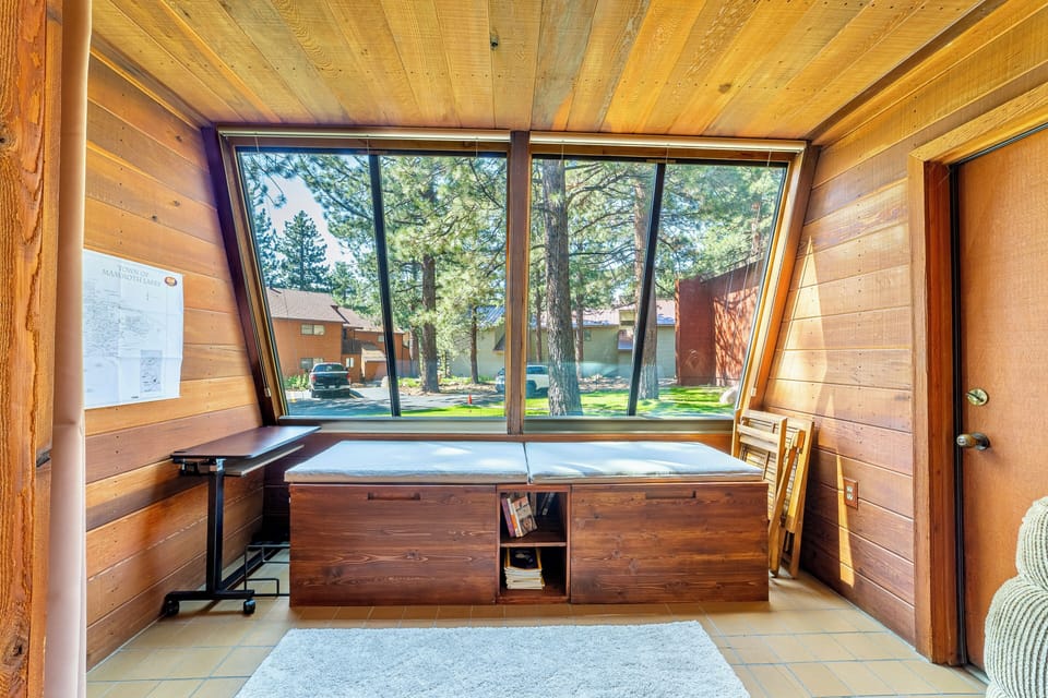 Sunroom with sitting area and large windows overlooking trees and grassy area.