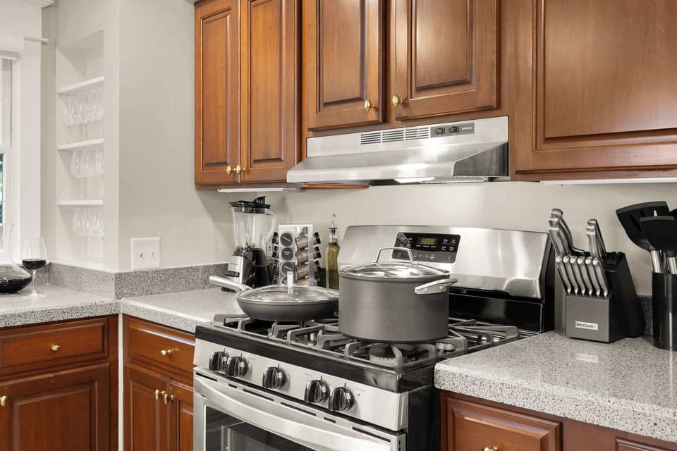 Well-equipped modern kitchen featuring stainless steel gas stove, full cookware set, countertop appliances, and open shelving with glassware—perfect for home-cooked meals.