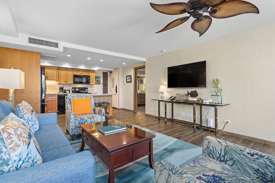 Your open-concept living space features coastal-blue furnishings, tropical ceiling fan, full kitchen, and flatscreen TV—perfect for unwinding after a day exploring paradise.
