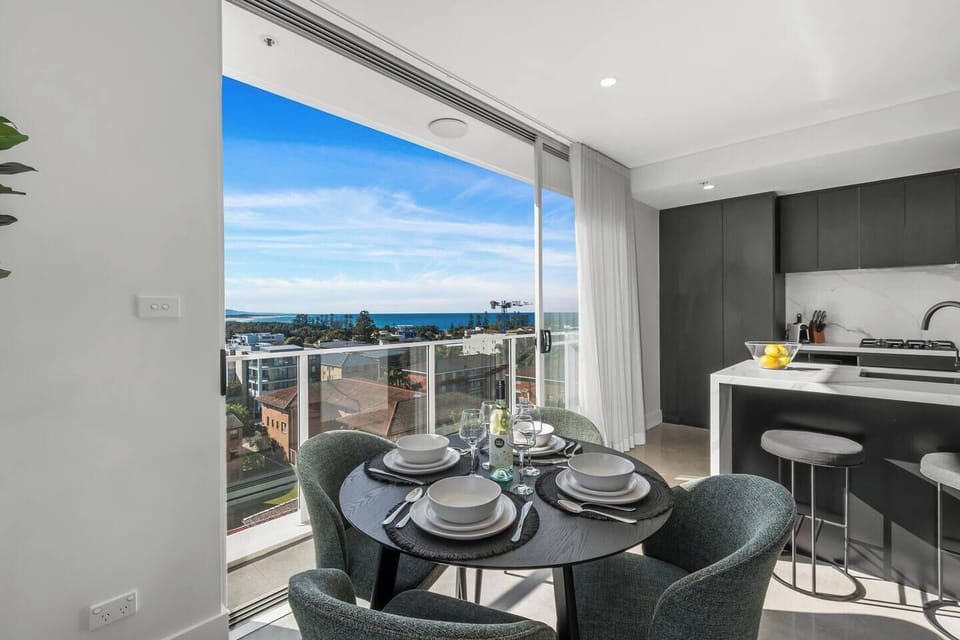 Gather at the dining table set against a backdrop of sea and sky—wine glasses, serving ware, and plush seating are all provided for stylish meals at home.