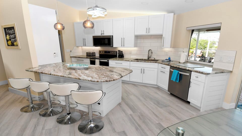 Modern fitted kitchen with large cooking island, white cabinetry, granite countertops and stainless steel appliances – stylish and functional