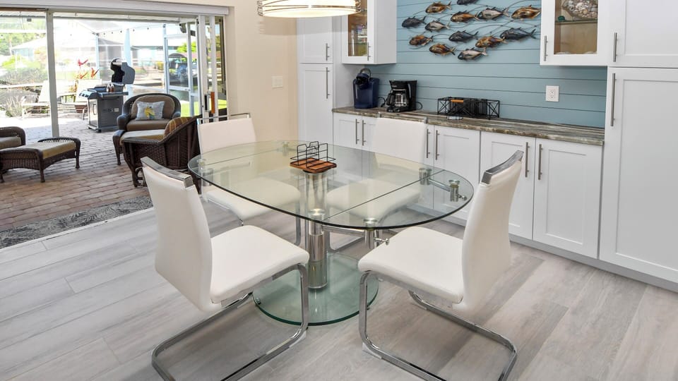 Modern dining area with glass table and white leather chairs, decorative fish sculpture and access to the terrace – stylish and full of light