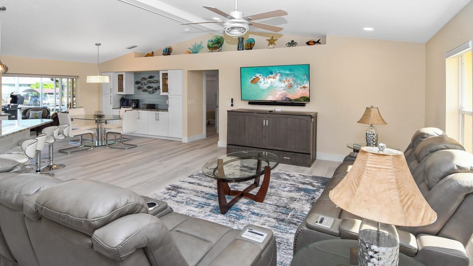 Bright open-concept living area with leather sofas, flat-screen TV, dining space and modern kitchen – stylish atmosphere with vacation vibes