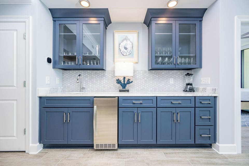 Enjoy preparing drinks and snacks at this stylish bar area, featuring navy cabinets with elegant glassware displays