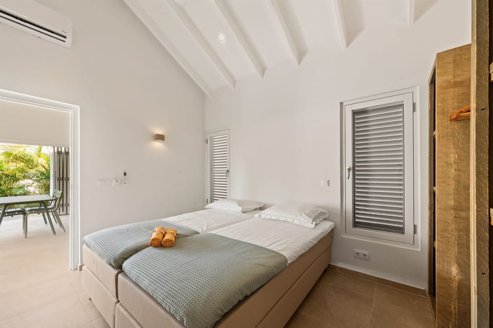Spacious twin bedroom with two Eastborn boxsprings (2.10 m), made up as separate beds. Features air conditioning, ceiling fan, and a private en-suite bathroom with a rain shower perfect for a restful stay in Curaçao’s Villa Blenchi.