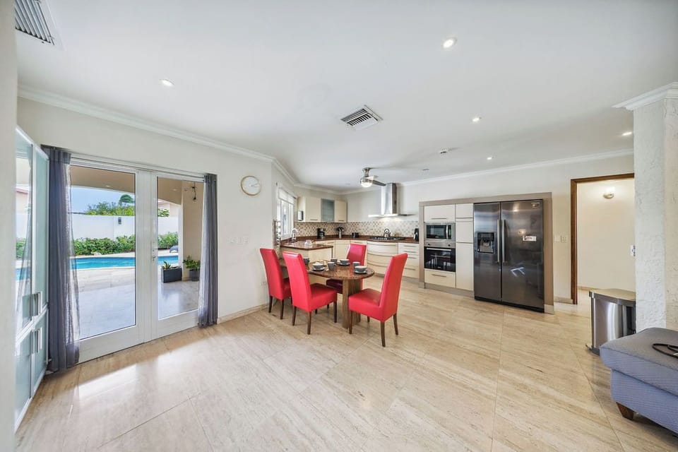 Gather around your dining table in this bright, modern space where the kitchen flows seamlessly into the open layout. Step through French doors to the sparkling pool just beyond your reach.
