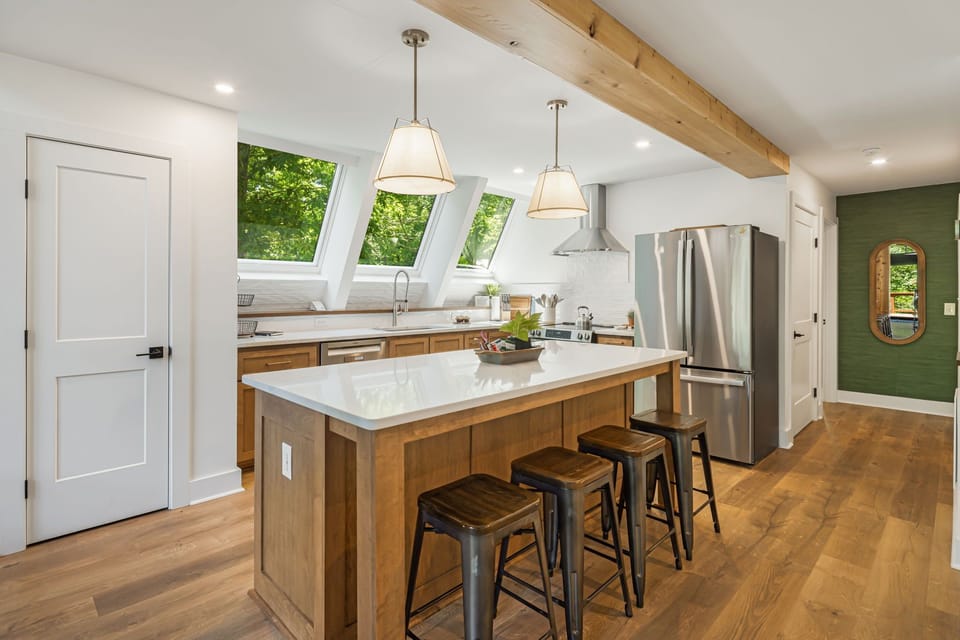 This modern and open kitchen with natural wood cabinets, quartz countertops and stainless steel appliances is fully stocked with cookware, utensils, and essentials to make meal prep a breeze. Skylights flood the space with natural light and nature views.