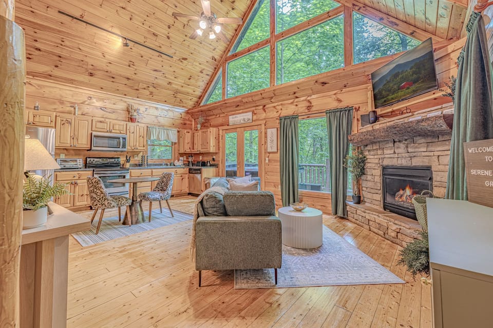 This stunning open-concept living area boasts soaring ceilings, a cozy stone fireplace, and expansive windows offering beautiful natural views.