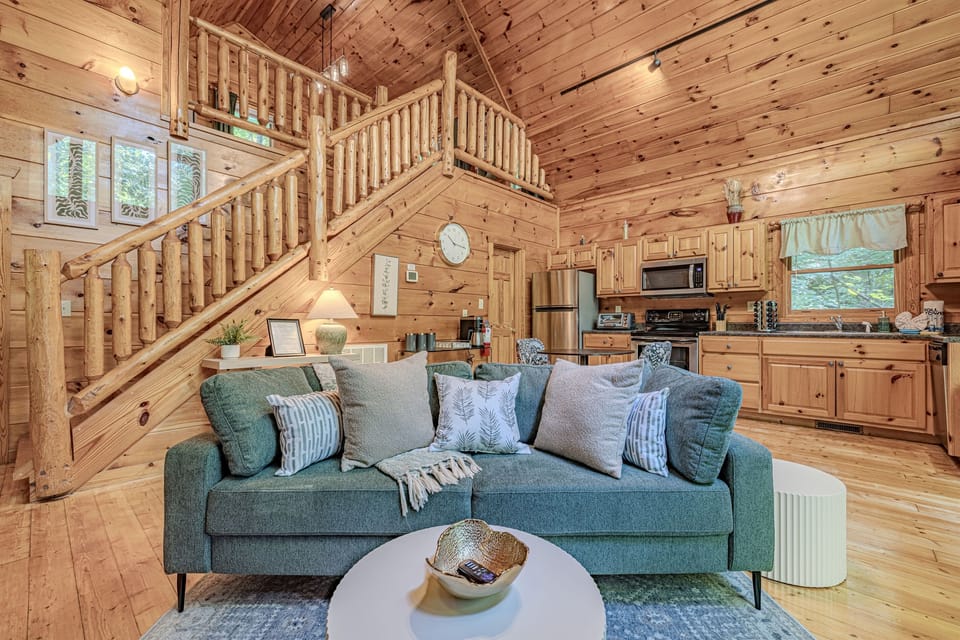 Relax in the comfortable living area, featuring a plush sofa and views of the cabin's open layout and rustic staircase.