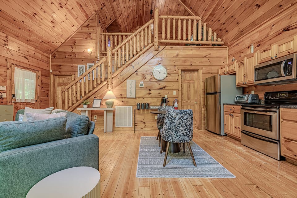 This inviting open-plan space seamlessly combines a fully equipped kitchen, a comfortable dining area, and a cozy living room, all beneath charming log cabin walls and a rustic staircase leading to additional levels. It's perfectly designed for gathering a