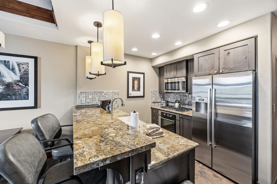 Kitchen peninsula with mosaic backsplash and gas range.