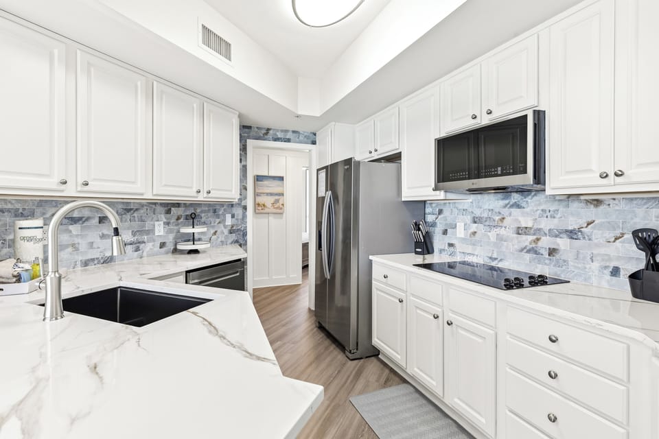 Your fully-equipped kitchen invites culinary adventures with sleek marble counters, stainless appliances, and beautiful coastal-inspired backsplash tiles.