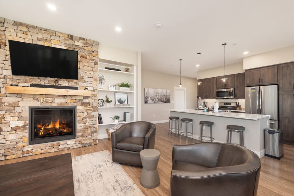 - Cozy stone fireplace with mounted TV and built in shelving for added charm and storage - Sleek open concept kitchen with stainless appliances and barstool seating - Warm lighting and leather seating create a stylish social hub