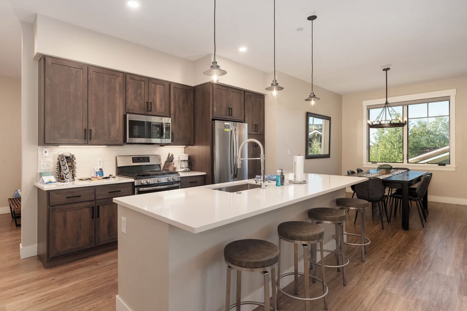 - Cook and connect in this sleek kitchen with quartz countertops and stainless appliances - Spacious island with four barstools offers the perfect spot for snacks or conversation - Pendant lighting and warm wood tones create a welcoming vibe