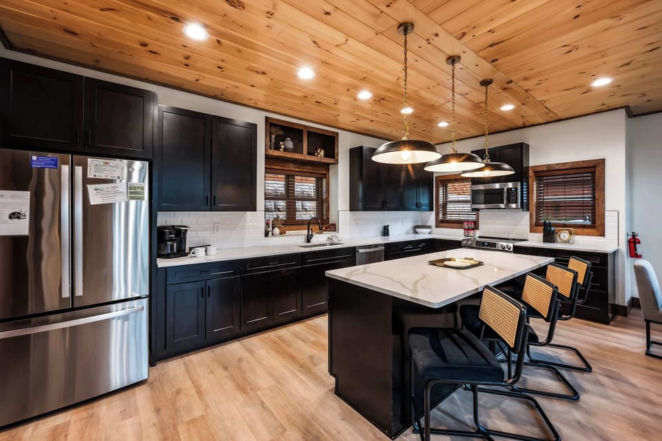 Modern kitchen with black cabinetry, a large island, and wood-paneled ceiling for a cozy atmosphere.