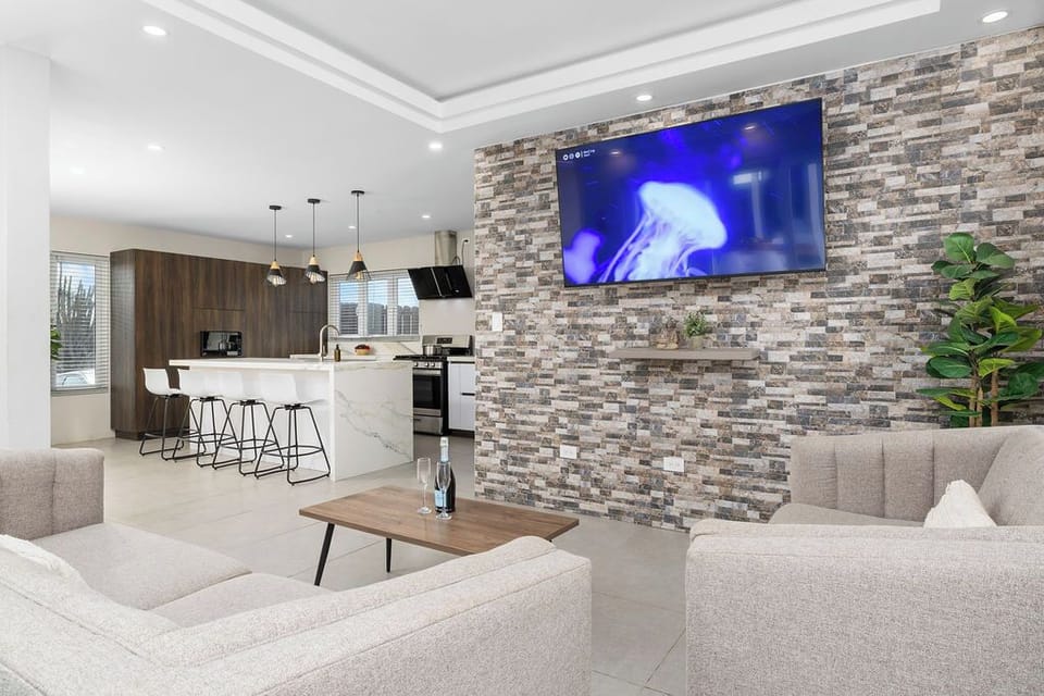 Spacious open-concept living area featuring a smart TV, cozy seating, modern island kitchen, and stylish stone accent wall—perfect for relaxing, cooking, and spending time with family or friends.