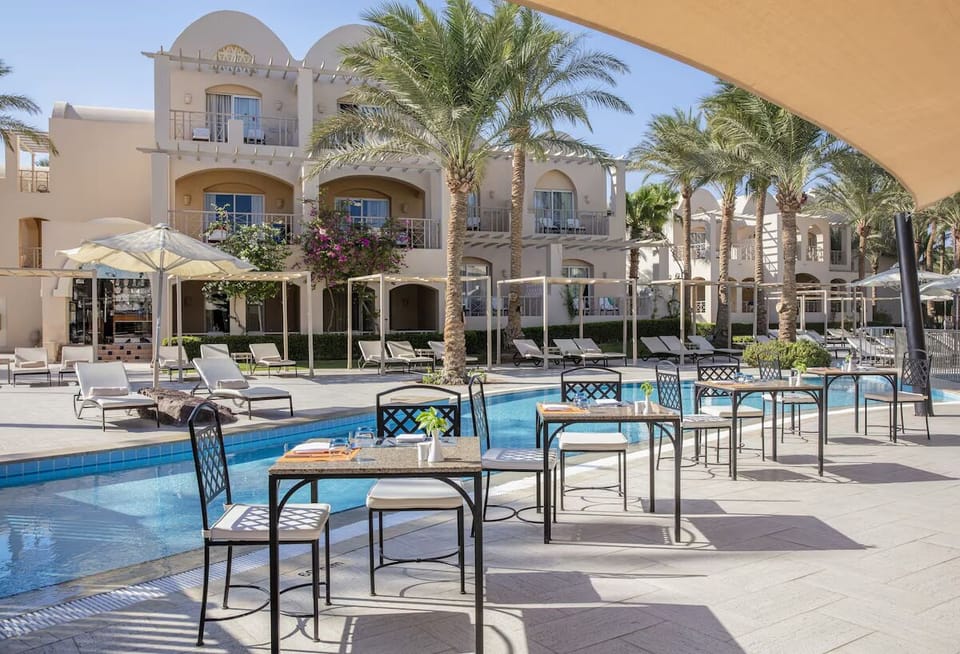 Lounge poolside with crisp cabanas, palms, and serene blue water.