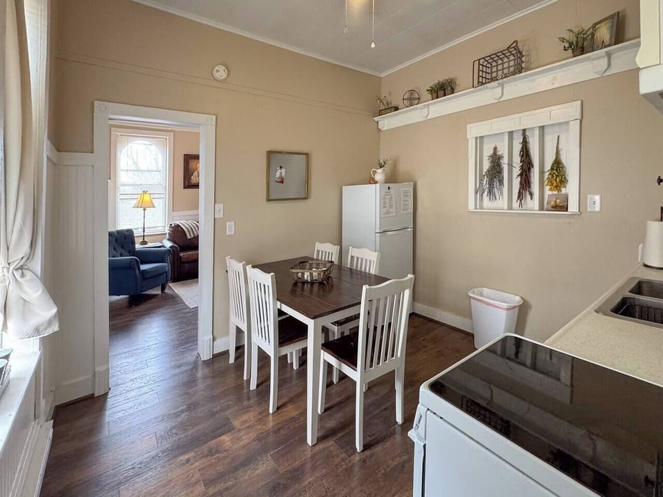 Depicts a dining area with a wooden table and chairs. There's a window with curtains.