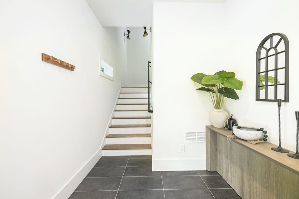 Bright entry hallway with stylish accents and natural wood stairs leading up to the main floor.