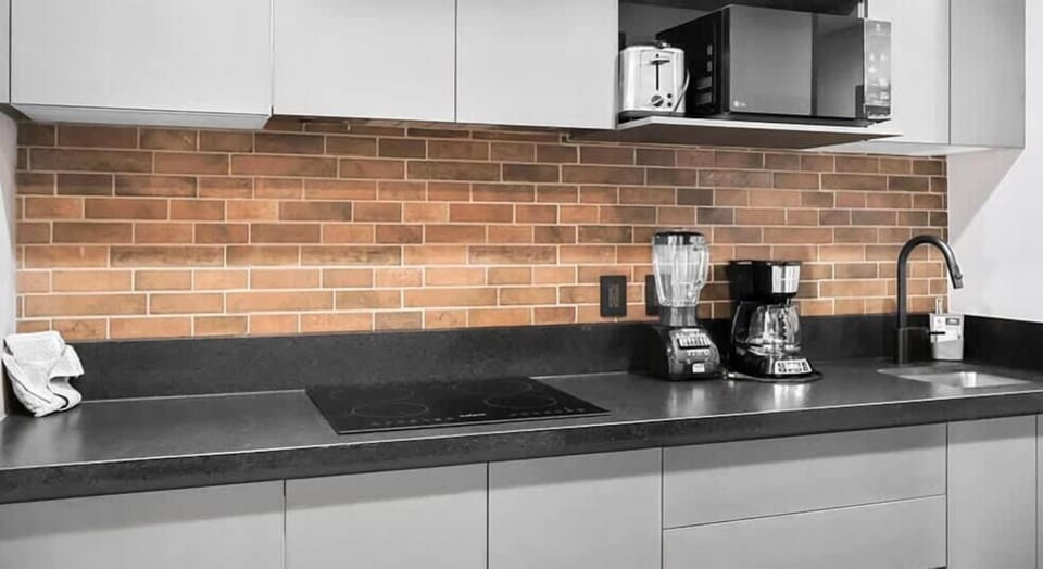 Sleek kitchen w/ dark counters, brick backsplash & modern appliances for easy cooking
