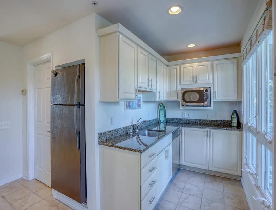 In the contemporary kitchen, elegant white cabinetry and granite countertops provide a stylish and functional space for meal preparation, with ample sunlight pouring in from the numerous windows.