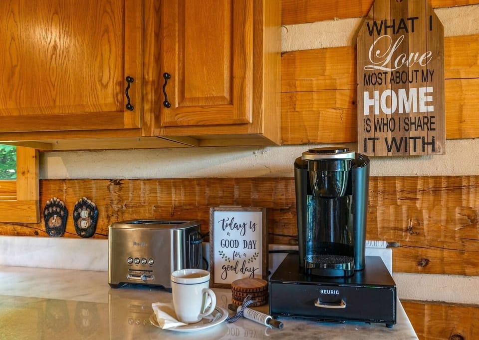 Cozy Kitchen corner with the coffee station. A toaster, Keurig coffee maker, and "Today is a Good Day" sign add to the warm vibe. View of greenery outside.