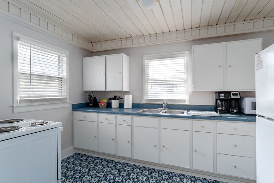 White kitchen with blue countertops, patterned floor, and two windows.