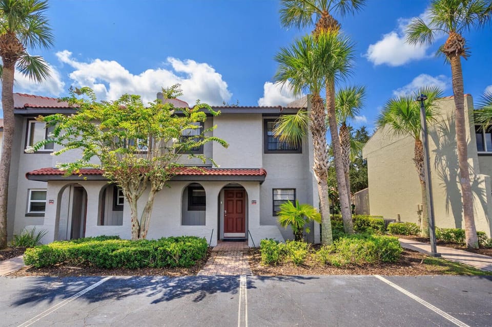 Exterior view of a townhouse with a red door and tropical landscaping under a clear blue sky.