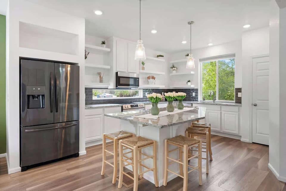 Spacious modern kitchen with granite island, stainless steel appliances, and stylish pendant lighting. Bright and airy with ample seating for gatherings. Perfect for cooking and socializing. Book your stay now for a comfortable, elegant experience!