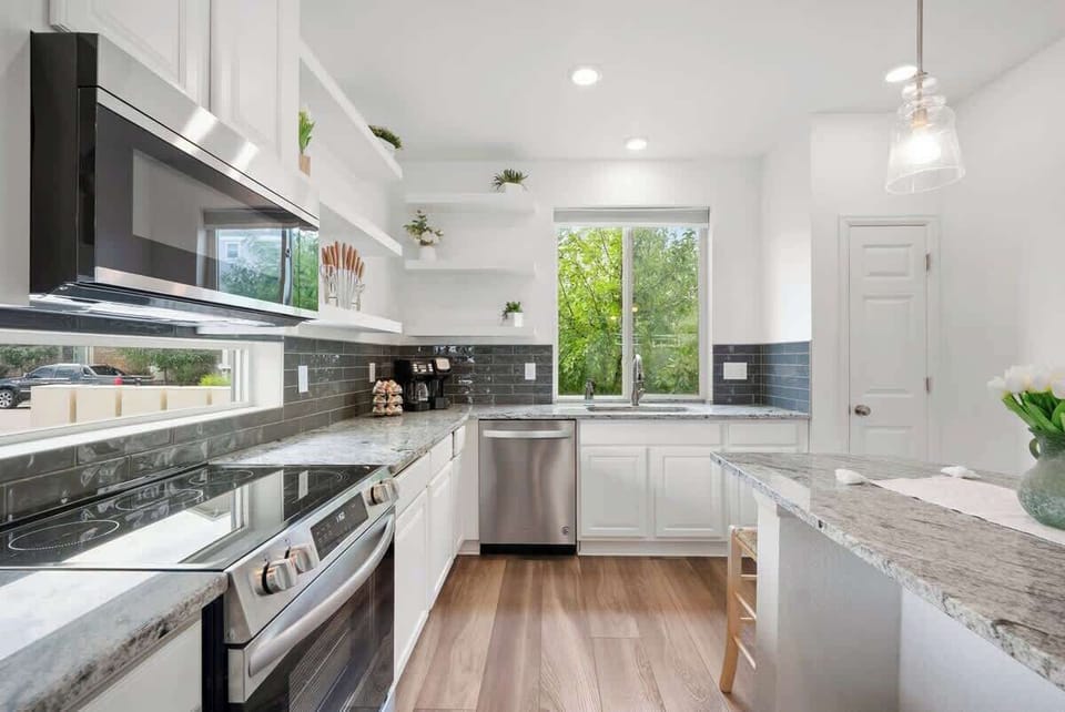 Bright modern kitchen with stainless steel appliances, granite countertops, and sleek white cabinetry. Spacious layout with natural light, perfect for cooking and dining. Enjoy a stylish, fully equipped kitchen during your stay. Book now for comfort!